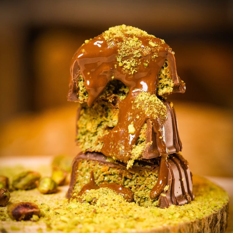 Stack of chocolate-covered pistachio desserts, drizzled with caramel and sprinkled with ground pistachios.