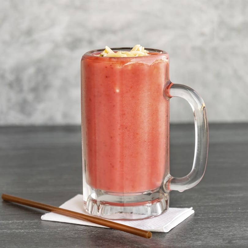 A Lebanese strawberry smoothie, topped with sliced almonds, in a glass mug with a straw.