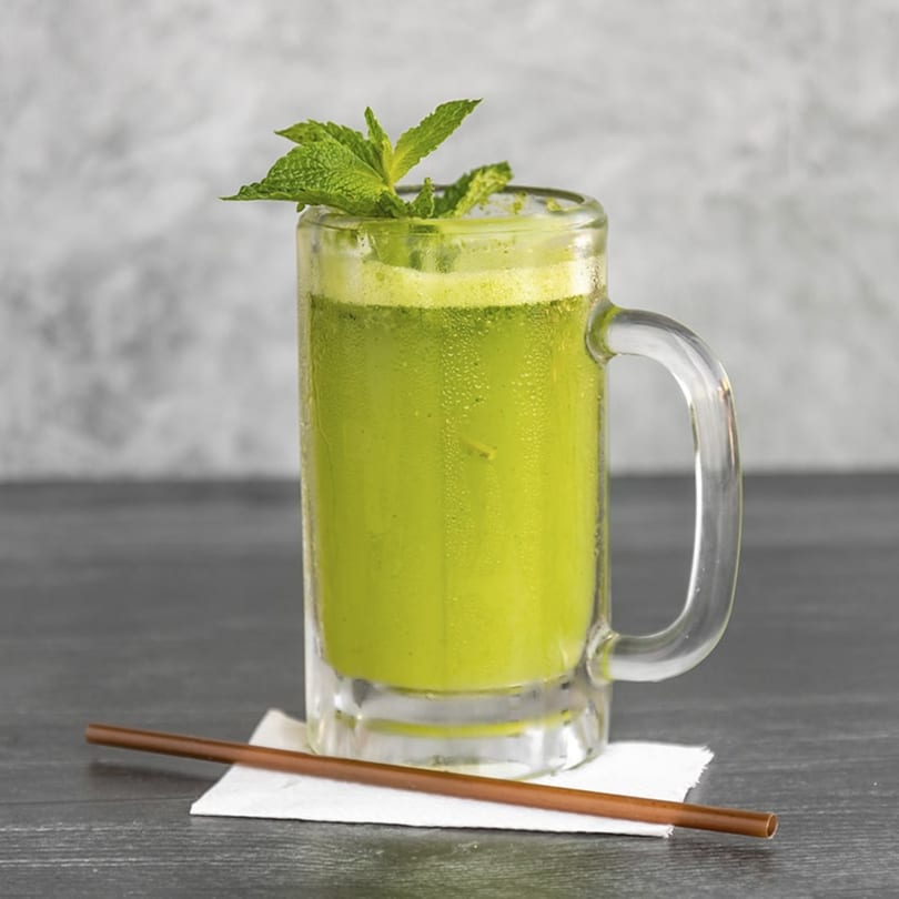 A frosty glass mug of vibrant green Lebanese mint lemonade, garnished with fresh mint leaves and a straw.