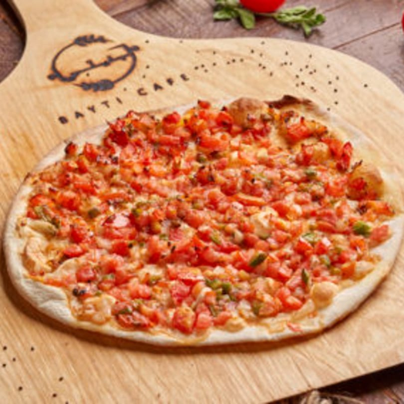 A Lebanese Manakish with diced tomatoes and herbs on a wooden serving board from Bayti Cafe.