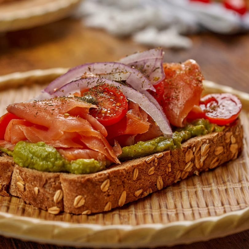 A close-up of a Bayti Cafe avocado toast with smoked salmon, red onions, and cherry tomatoes.